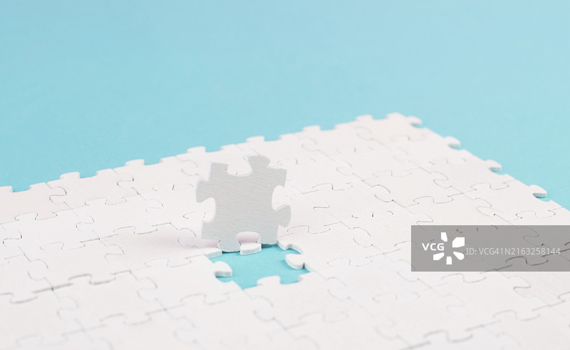 蓝色背景上的白色拼图，缺失部分，团队合作寻找解决方案，最后一块图片素材