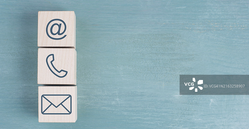 木块上的电子邮件、电话和新闻简报标志，蓝色背景，文本的复制空间，业务支持和沟通概念图片素材