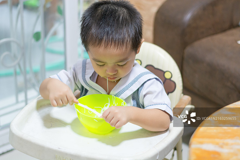 坐在高脚椅上自己吃饭的亚洲男婴图片素材