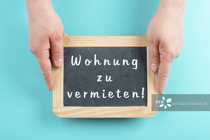 手拿黑板，上面用德语写着公寓出租，搬到新家，房地产图片素材