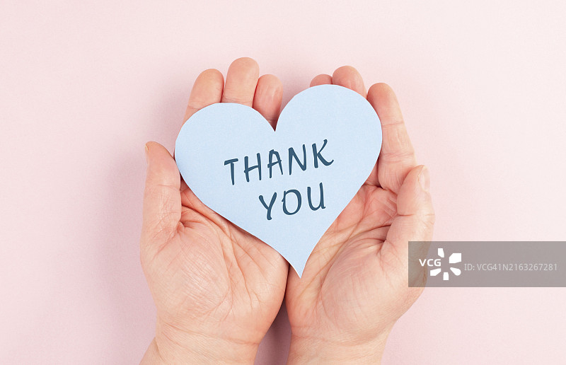 手捧写有“谢谢”的心，粉色背景感恩卡片图片素材