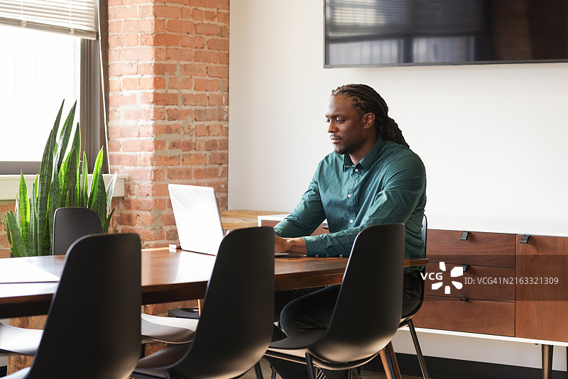一位留着脏辫的非裔美国商人穿着休闲装，用笔记本电脑工作图片素材