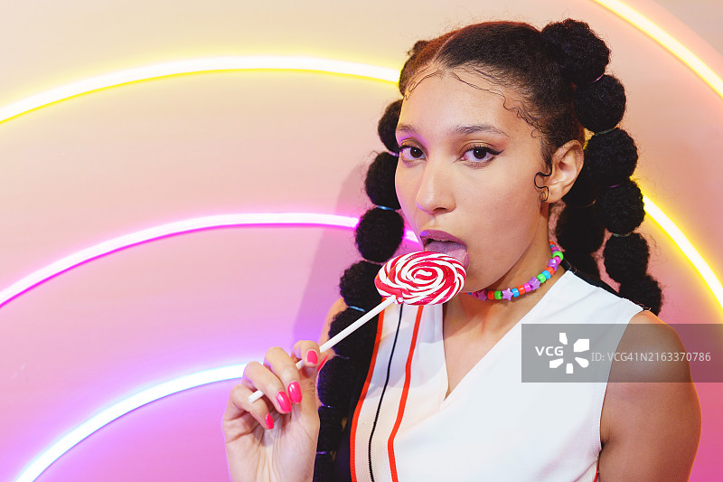 在彩色背景下吃糖果的混血女子肖像图片素材