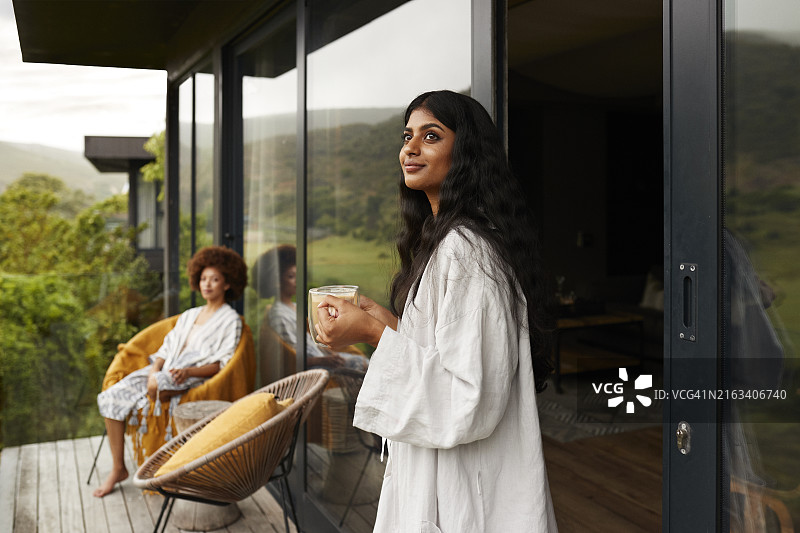 在阳台上，年轻女人端着咖啡杯与女性朋友聊天图片素材