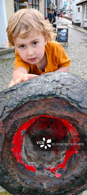 攀爬旧炮筒的金发白人男孩特写图片素材