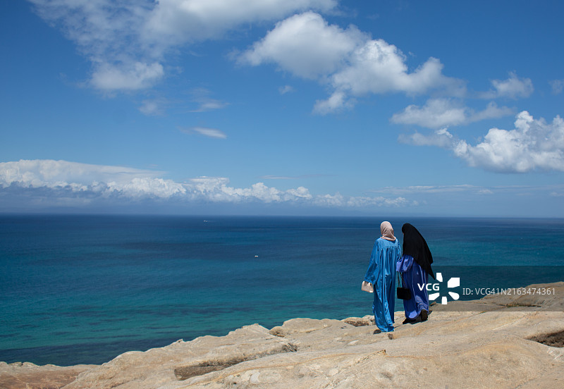 两位穿着蓝色传统吉拉巴长袍的穆斯林妇女在摩洛哥丹吉尔看海图片素材
