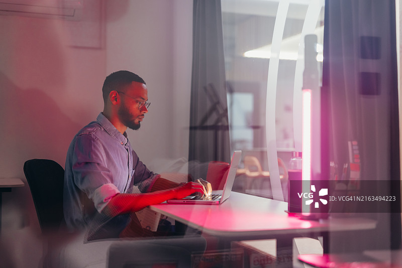 衬衫眼镜男：夜晚在办公室用笔记本电脑工作图片素材