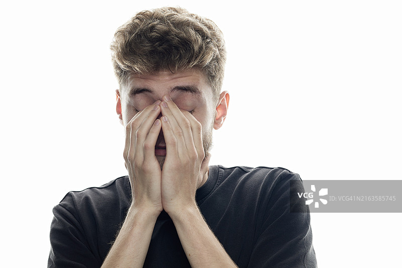 在休闲工作室拍摄中，面带微笑用手遮住脸的年轻男人图片素材