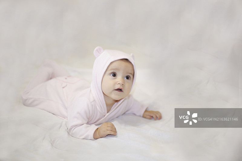 穿着粉色连体衣的宝宝躺在柔软的白色表面上图片素材