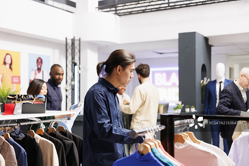 服装店衣架上的衣服和购物的顾客图片素材