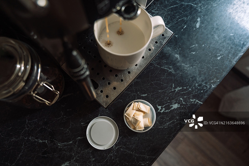 咖啡机将咖啡注入白色马克杯，旁边是打开的鼻烟罐图片素材