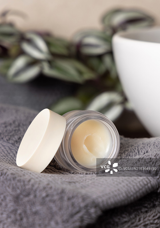 深灰色毛巾上的已打开润唇膏罐，浴室木质植物和洗手盆附近样机图片素材