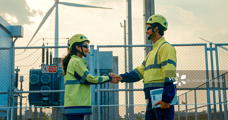 可再生能源工程师在工厂握手，象征着与风力涡轮机的成功协议或伙伴关系。绿色生态发电风能可持续能源。图片素材