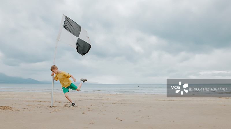 男孩在广阔的海滩上挥舞黑白格子旗跳舞图片素材