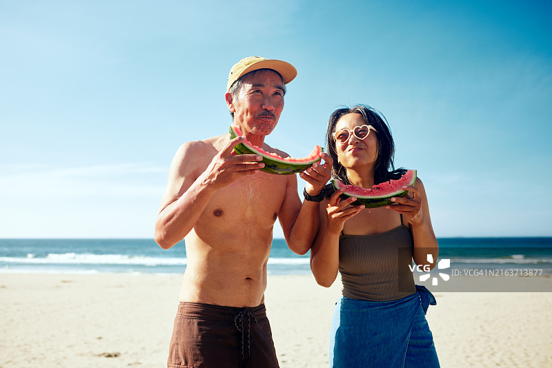 一对男女穿着泳衣在夏季海滩上啃西瓜。图片素材
