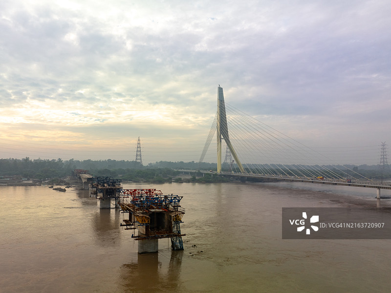 4K无人机视角:新德里标志性大桥日落时分的金色时刻,2023年7月印度新德里亚穆纳河洪水泛滥,桥下可见浑浊的河水图片素材
