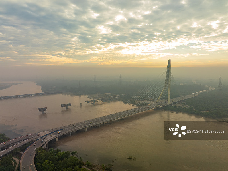 4K无人机视角:新德里标志性大桥日落时分的金色时刻,2023年7月印度新德里亚穆纳河洪水泛滥,桥下可见浑浊的河水图片素材