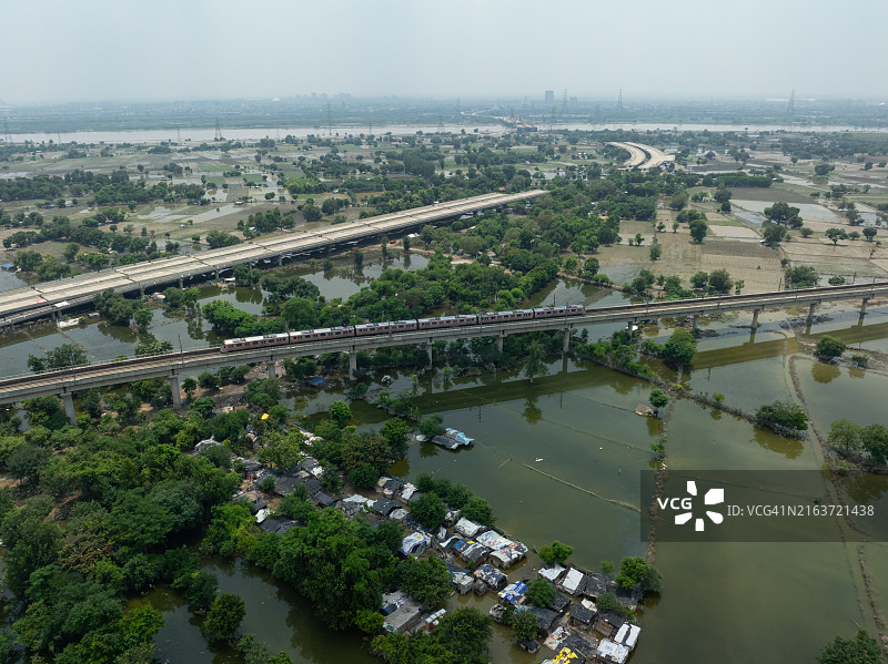 印度新德里高架铁轨上的德里地铁列车鸟瞰，阿克夏达姆神庙附近的洪水农田图片素材
