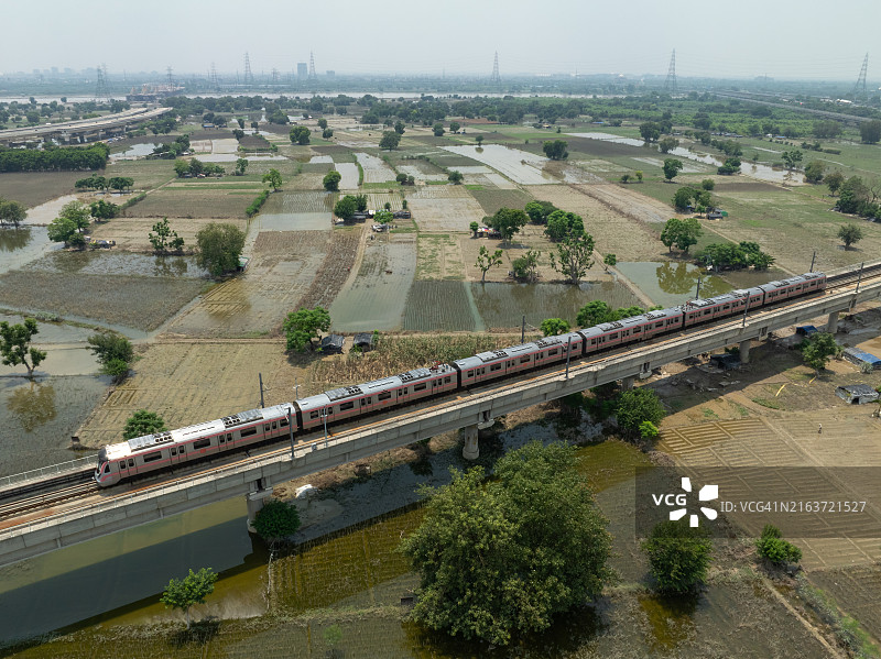 印度新德里高架铁轨上的德里地铁列车鸟瞰，阿克夏达姆神庙附近的洪水农田图片素材