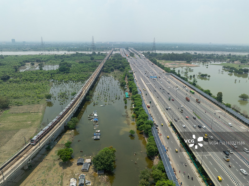 印度新德里高架铁轨上的德里地铁列车鸟瞰，阿克夏达姆神庙附近的洪水农田图片素材