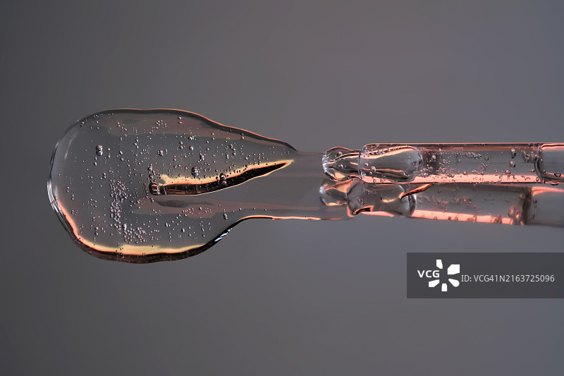 在带有橙色色调的深色背景上，带有流动的血清的移液器图片素材