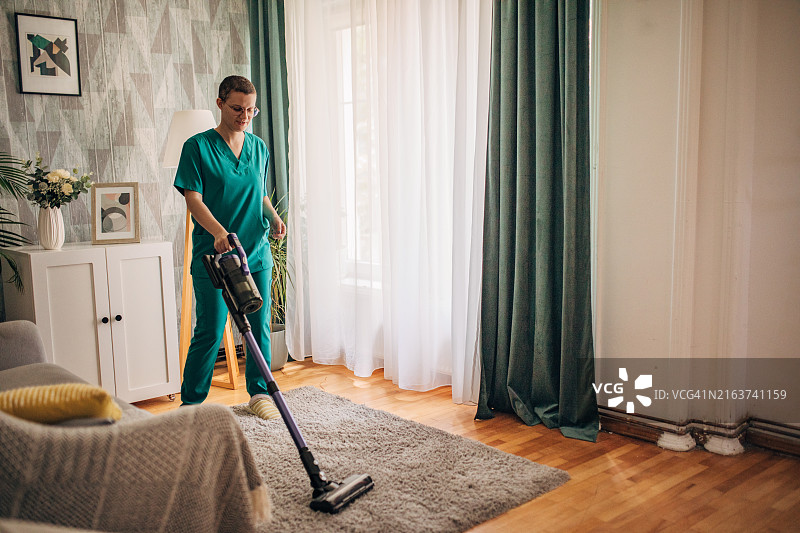 用真空吸尘器清洁带有绿色窗帘和地毯的现代客厅。图片素材