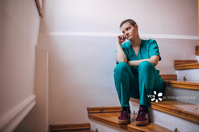 穿绿色手术服的白人短发护士，坐在楼梯上哭泣。图片素材