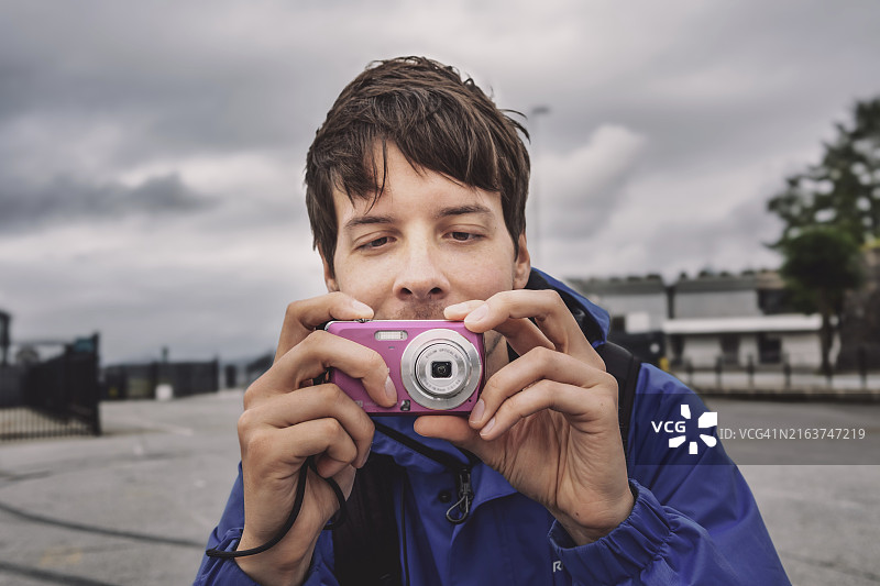 留着棕色头发的年轻男子用复古粉色数码相机拍照图片素材