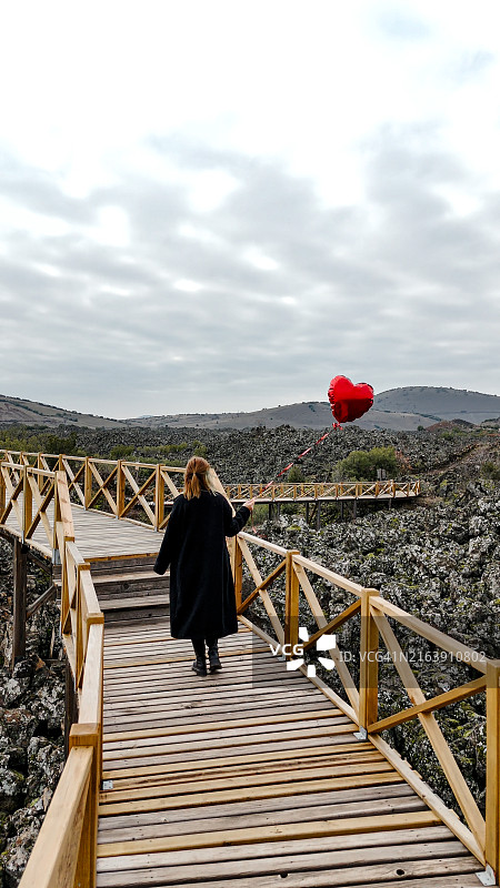 马尼萨库拉萨利赫利联合国教科文组织世界地质公园和火山公园以及Divlit Tepe火山群空中鸟瞰，位于库拉火山地质公园，一位悲伤的年轻女子手拿红色气球走过图片素材