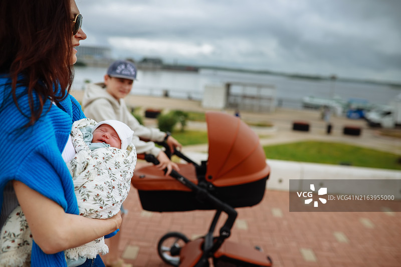 妈妈抱着新生儿，哥哥推着婴儿车图片素材