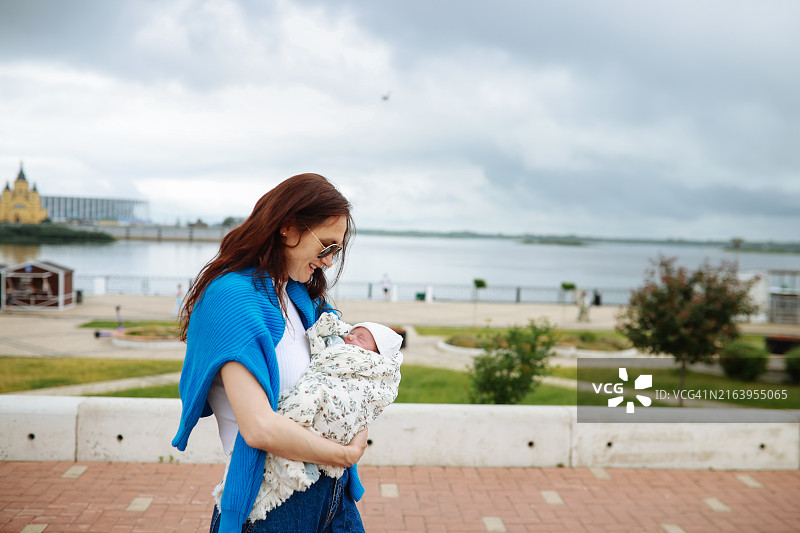时尚中年妈妈抱着新生女儿在城市滨水区散步图片素材