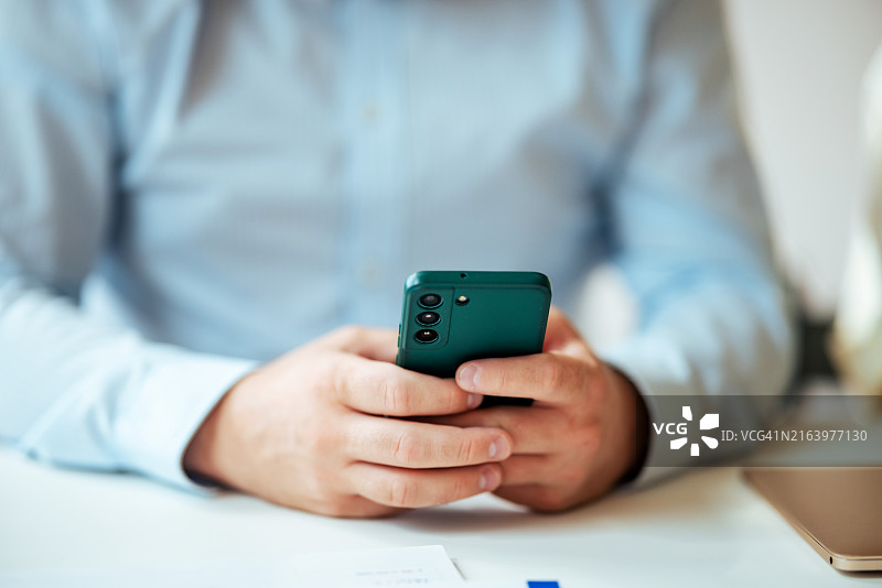 在办公室环境的办公桌前使用智能手机的商人图片素材