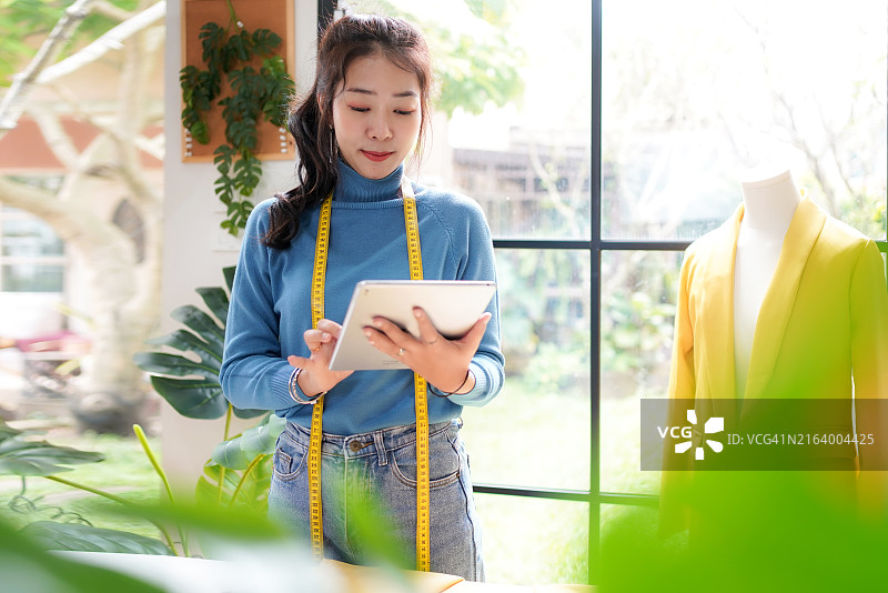 年轻女服装设计师在展厅使用笔记本电脑工作并接收客户的设计订单图片素材