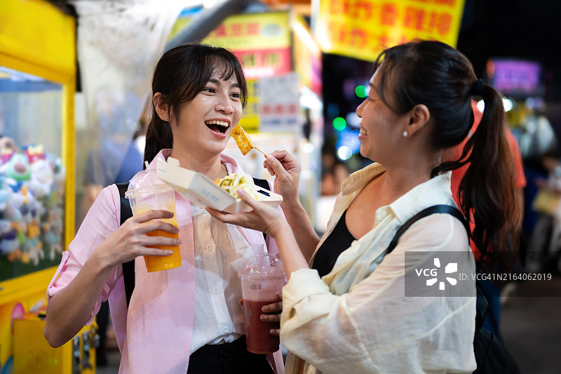 两名中国台湾女性游客在台北西门町夜市品尝美味的臭豆腐图片素材