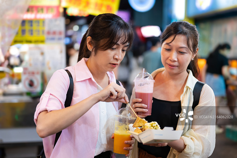 两名中国台湾女性游客在台北西门町夜市品尝美味的臭豆腐图片素材