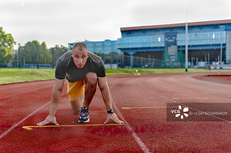 年轻男人准备在日落时分的田径场上冲刺图片素材