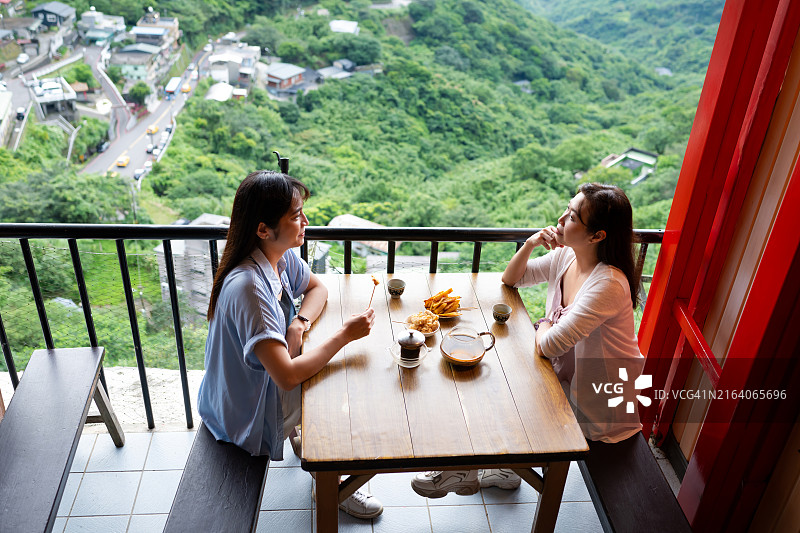 两位女游客在中国台湾九份老街的迷人景点品尝小吃和中国茶，欣赏壮丽的自然风光图片素材