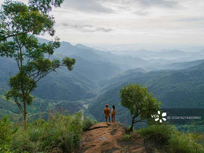 站在埃拉岩石上眺望葱郁绿色山丘的男人和女人的鸟瞰图图片素材