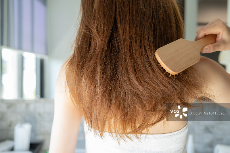 年轻的亚洲女性用梳子梳理浓密头发的背影图片素材