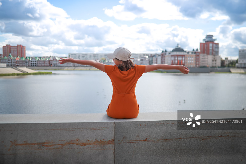 城市探索：少女在水泥护墙上欣赏湖景，旅行图片素材