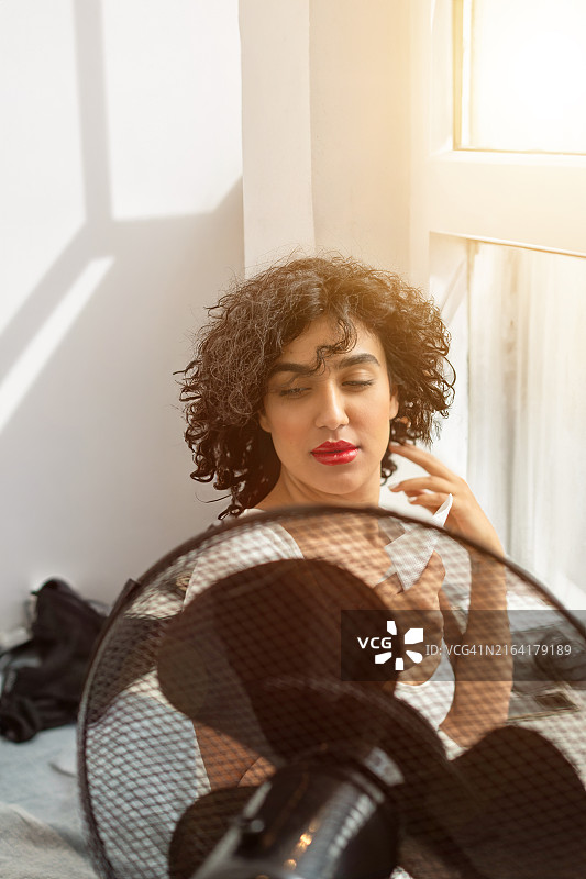 在晴天里，于风扇前试图降温的女人图片素材