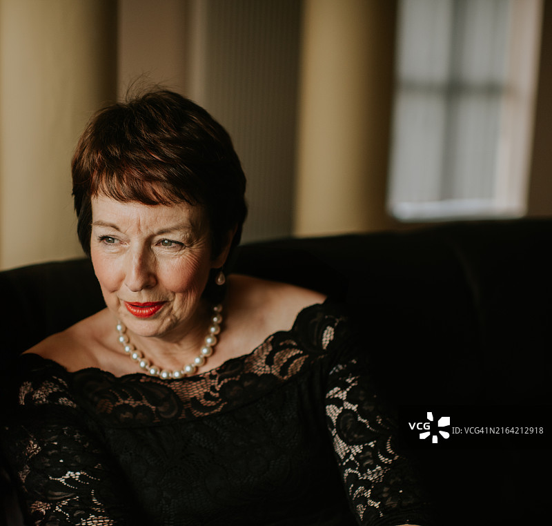 身穿黑色蕾丝连衣裙，在沙发上摆姿势的优雅女人，柔和的光线图片素材