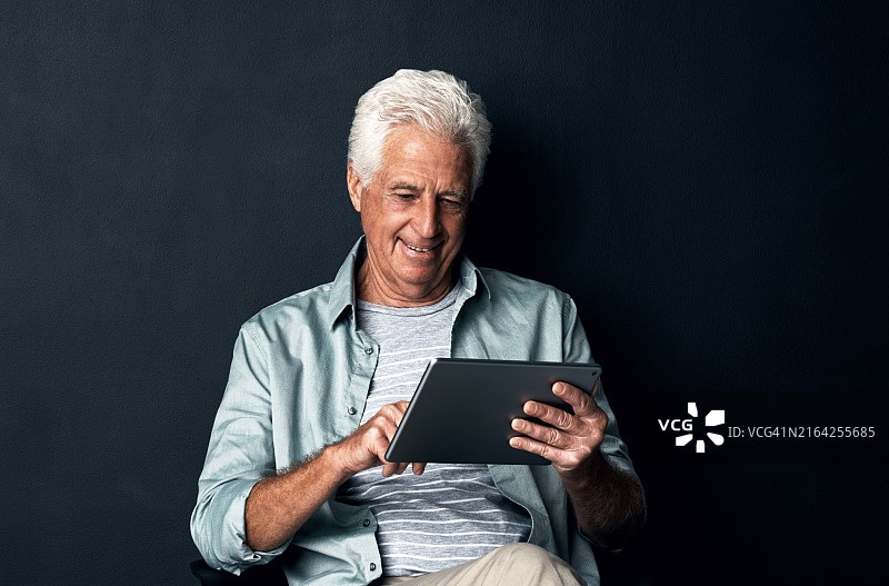 老年男人在黑色背景下使用平板电脑的影棚照片图片素材
