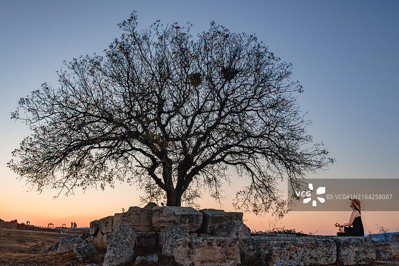 漂亮女人在吕克斯河畔的老底嘉古遗址中，在美丽的树旁冥想，做瑜伽图片素材