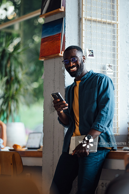 在舒适的咖啡馆里使用智能手机的微笑男人图片素材