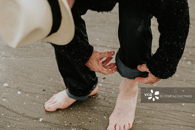 年长的男人在日落时分赤脚走在沙滩上，卷起裤腿图片素材
