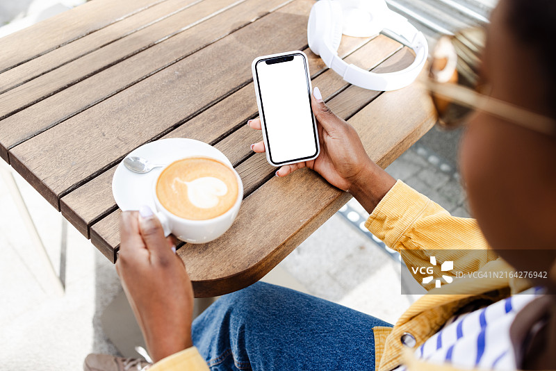 女人坐在自助餐厅里，一边喝咖啡一边使用带有空白屏幕的智能手机图片素材