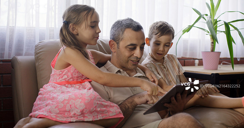 父女和儿子在家中使用平板电脑，享受家庭时光图片素材