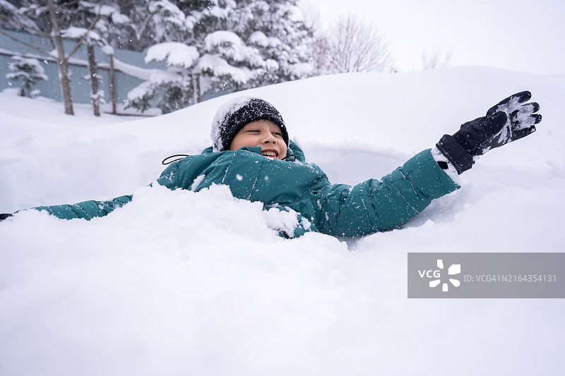 韩国男孩在蓬松的白雪上露出调皮的笑容，享受冬季和雪带来的喜悦图片素材