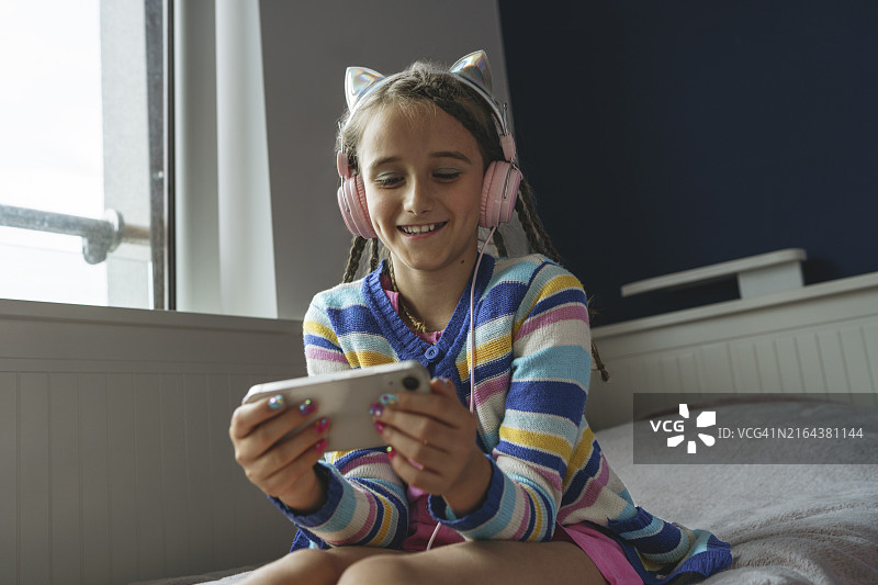 快乐的女孩戴着耳机在家用手机看电影图片素材